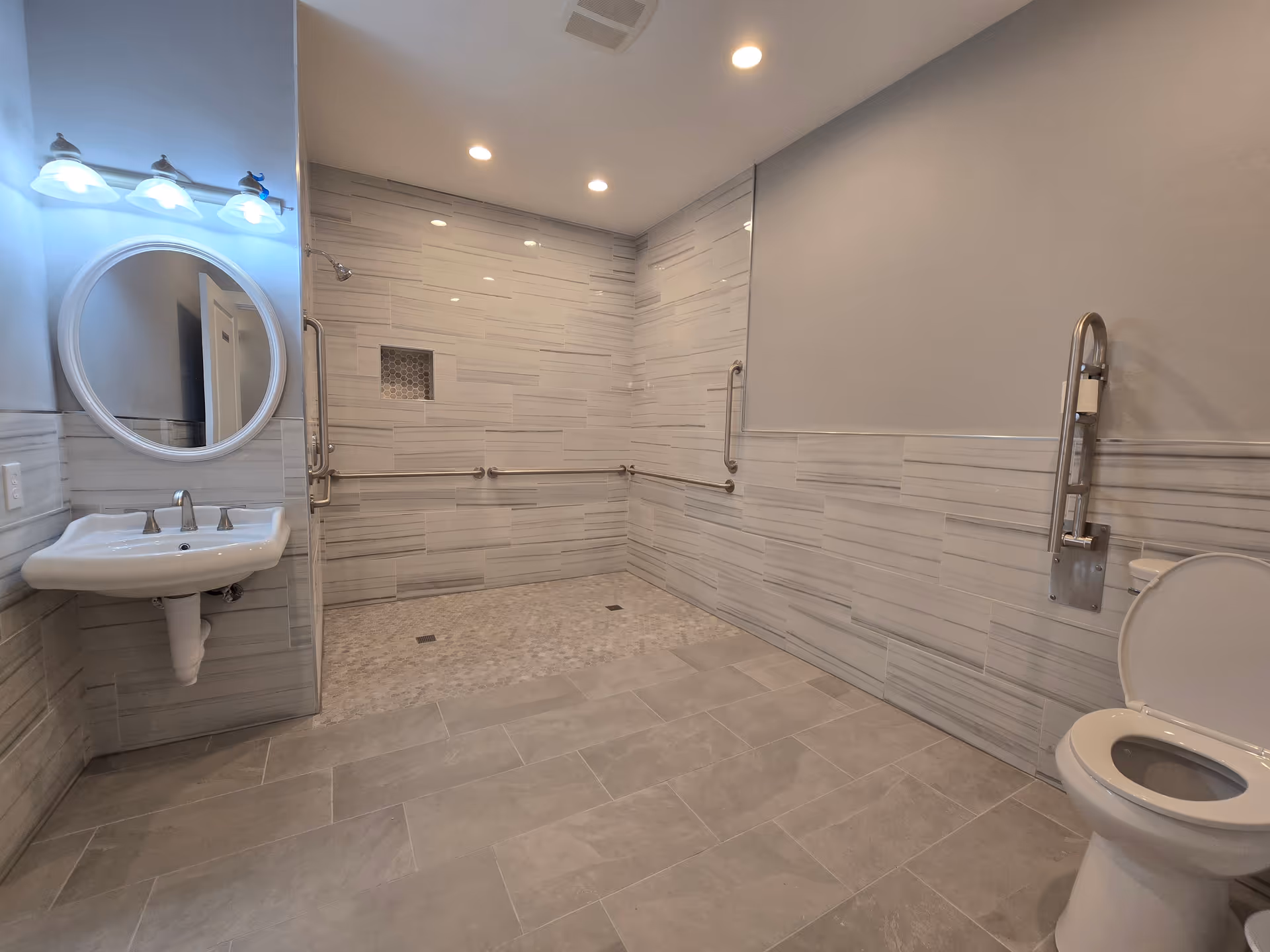 Accessible bathroom featuring sink, mirror, toilet, and a walk-in shower with grab bars.