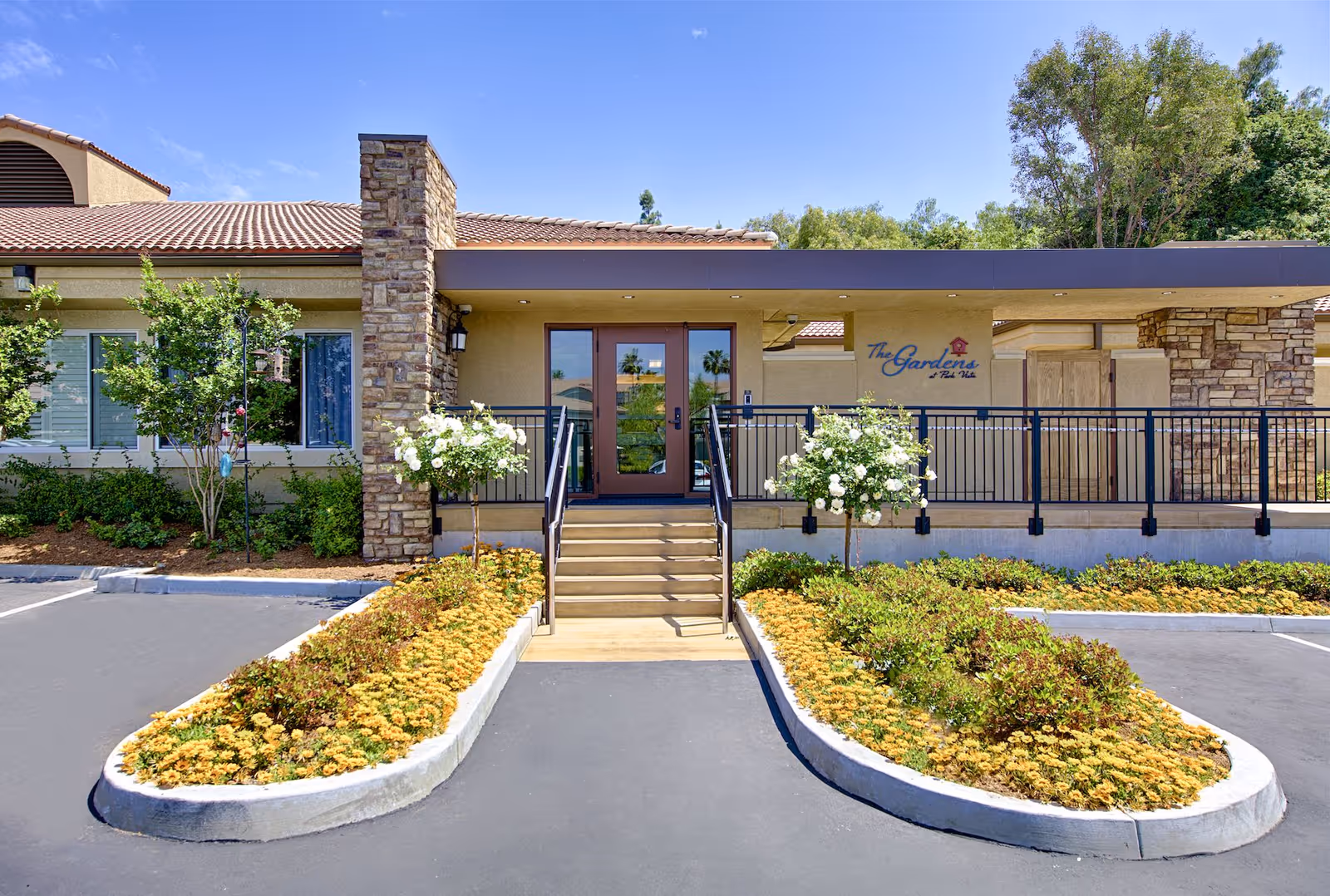 A brick-and-stone senior living facility entrance surrounded by landscaped planters.