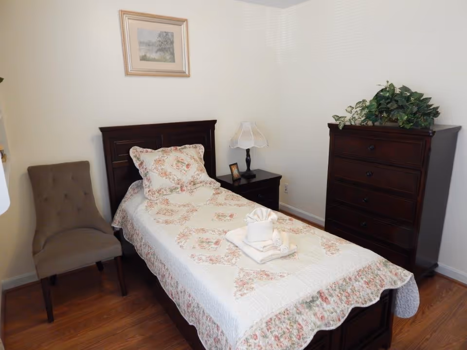 Single bed with floral quilt, nightstand, chair, and dresser in a cozy bedroom.