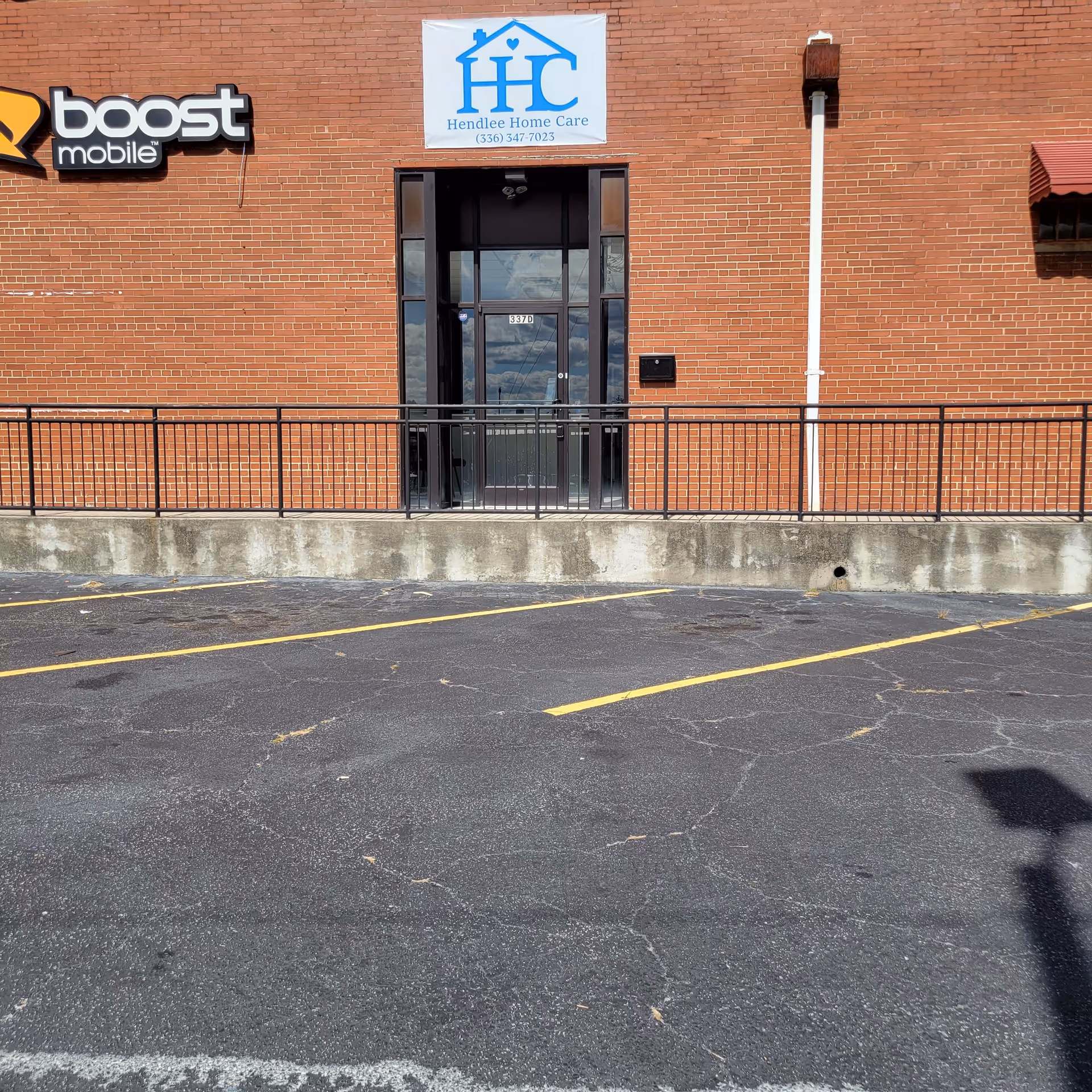 Exterior brick building with Hendlee Home Care sign, glass entrance, and parking lot.