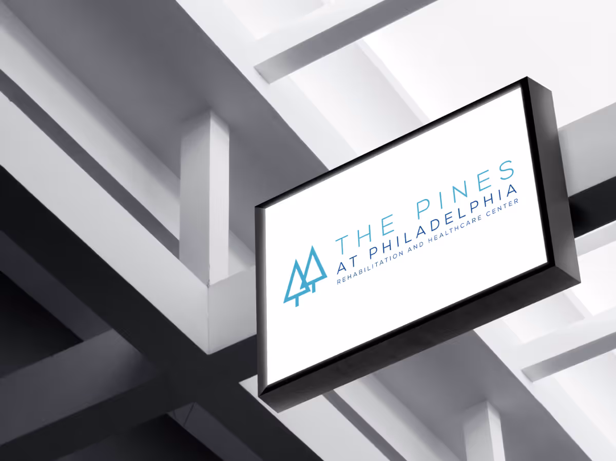 A rectangular sign reading The Pines at Philadelphia Rehab and Healthcare Center hanging from ceiling beams.