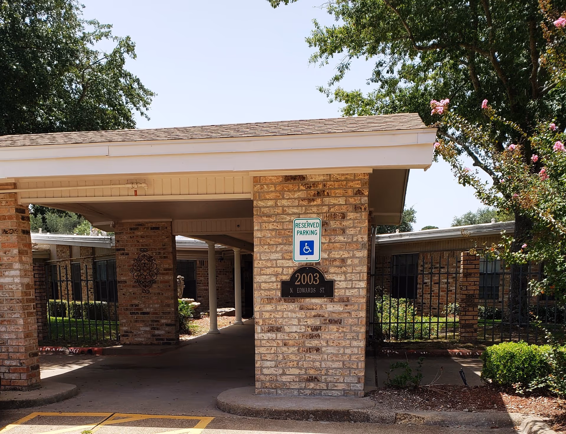 Brick building entrance with a covered driveway, handicap parking sign, and address plaque.