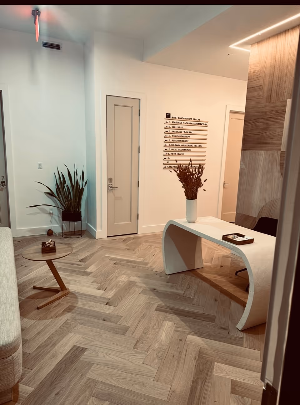 Reception area featuring a curved white desk, round side table, tall plant, and directory sign.