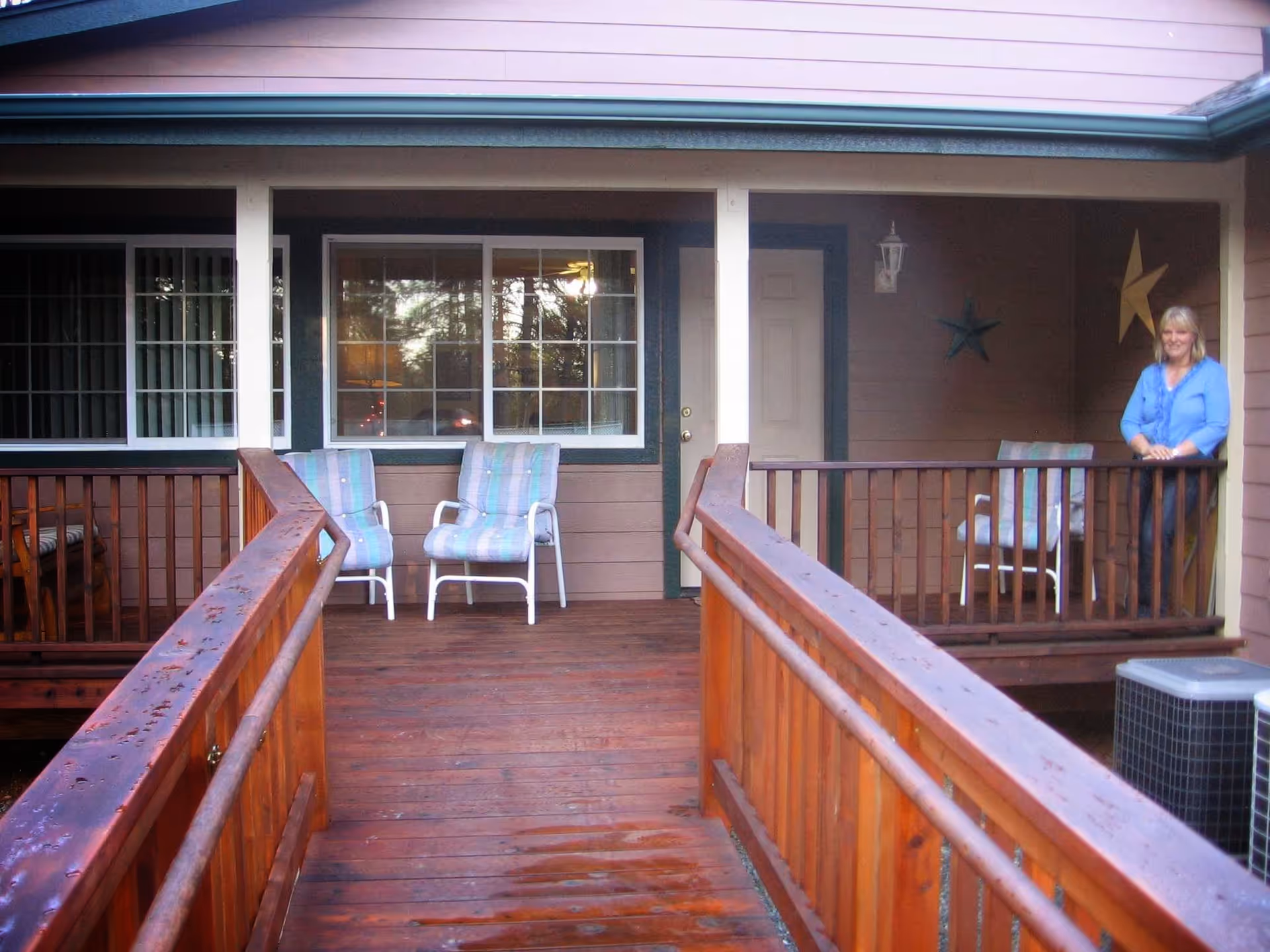 Wooden porch with chairs overlooks a building front; a woman stands at the railing.