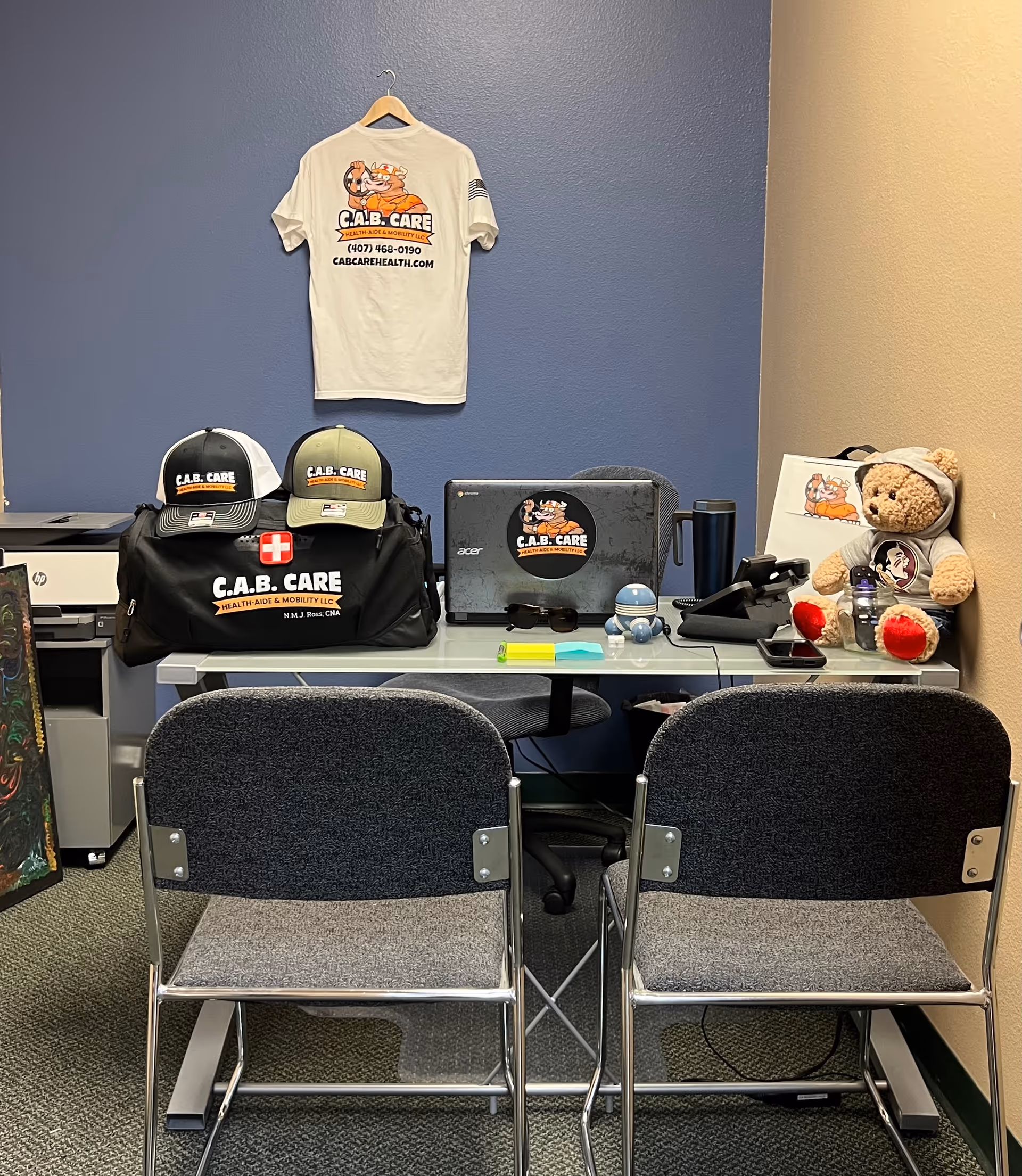 Interior office desk with CAB Care branding, hats, a laptop, bags, and a teddy bear.