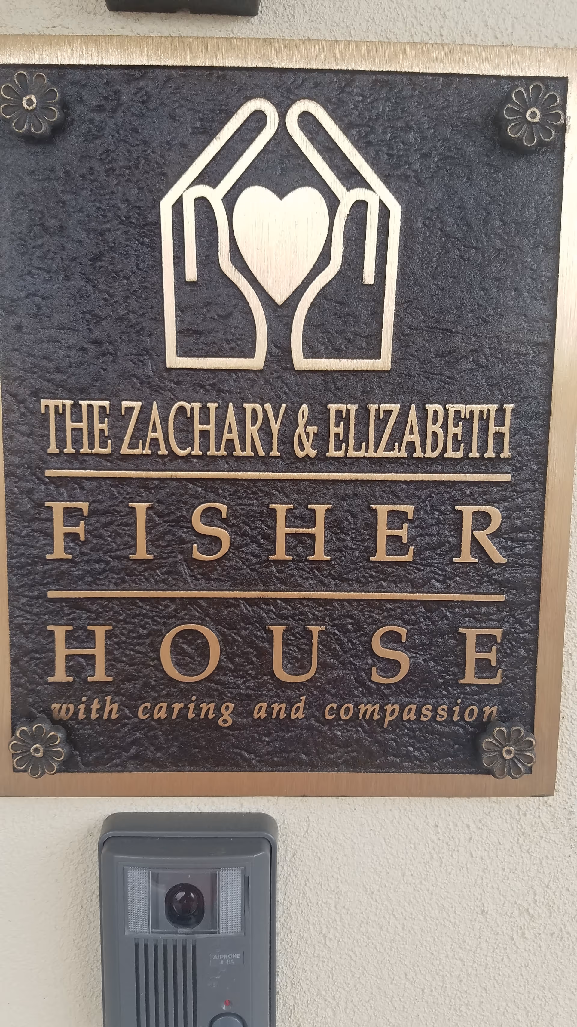 Exterior wall plaque reads The Zachary & Elizabeth Fisher House with caring and compassion logo.