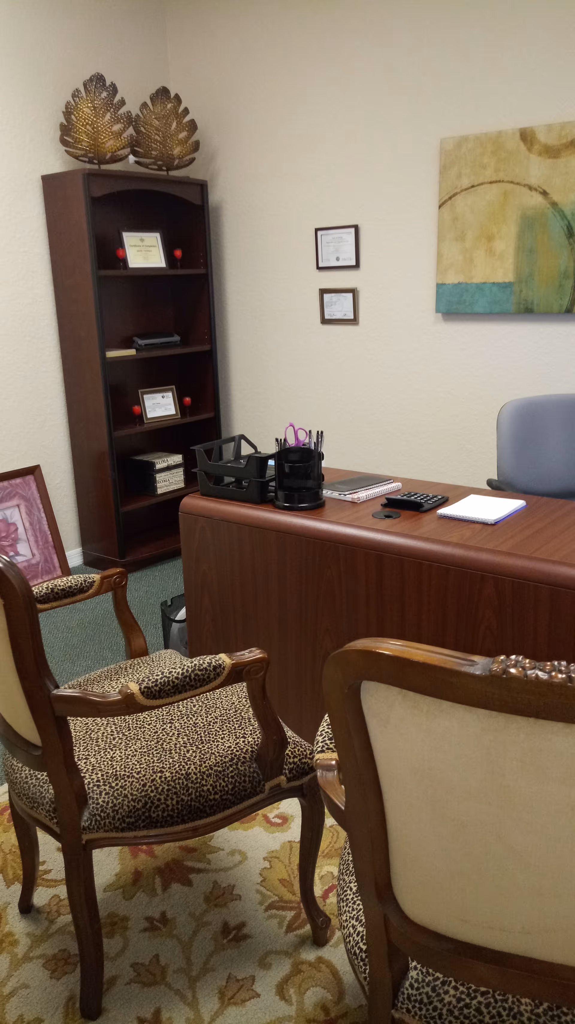 Interior office/reception area with wooden desk, chairs, bookshelf, and wall art.