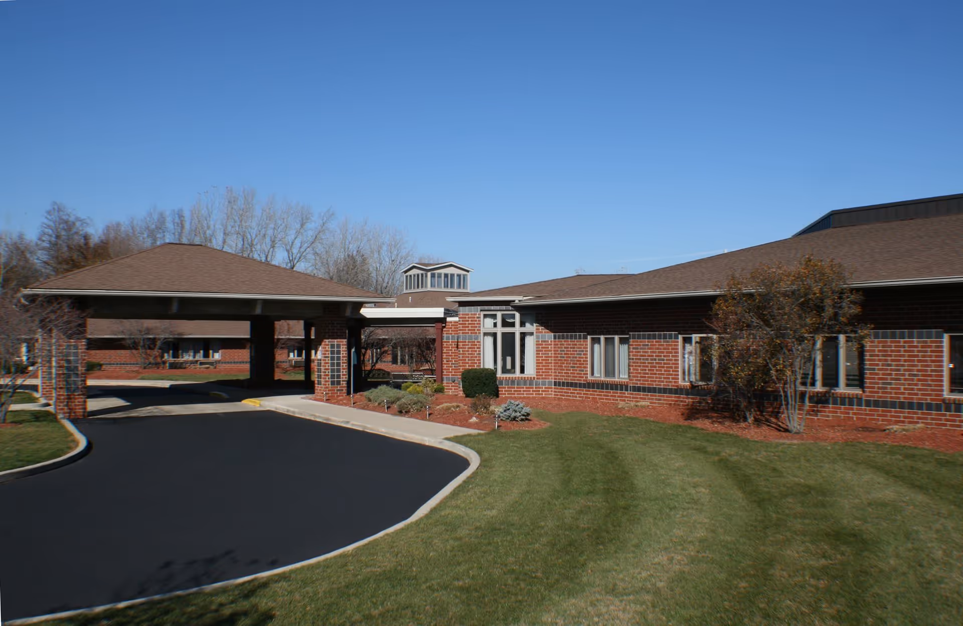 Brick senior living facility exterior with driveway, portico, and manicured lawn