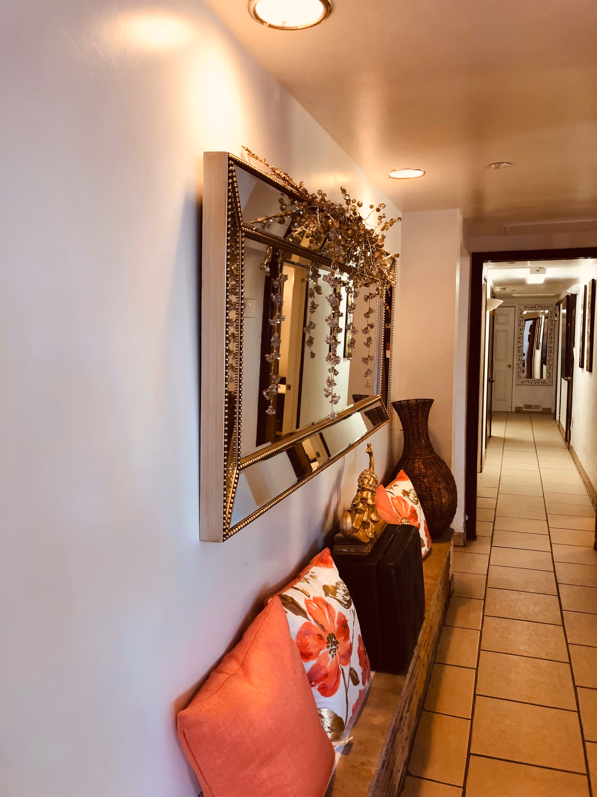 Narrow hallway with tiled floor, wall mirror, and decorative seating along the wall.