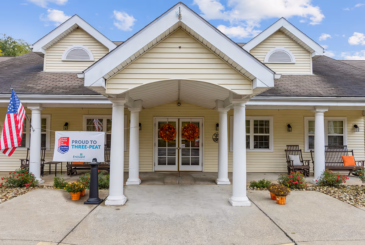 Beige senior living facility entrance with white columns, a covered porch, and an American flag.
