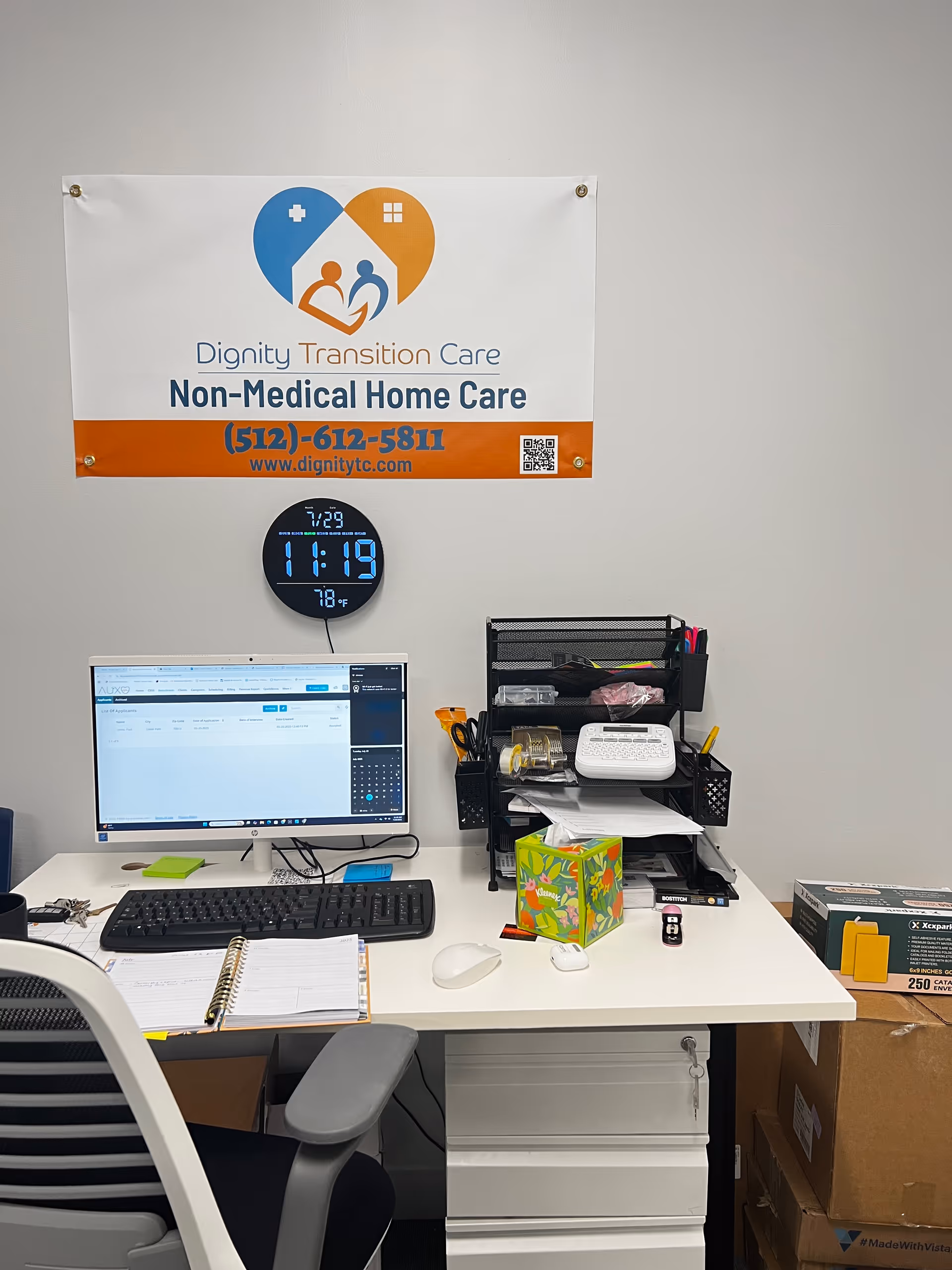 Office desk with computer setup, clock, and banner reading Dignity Transition Care Non-Medical Home Care.