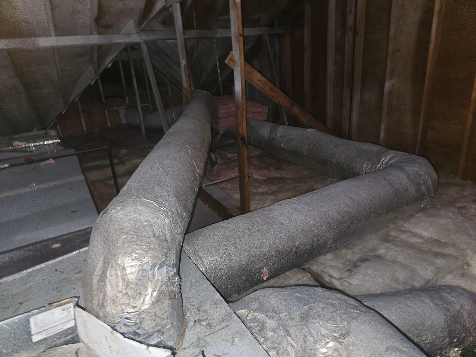 Unfinished attic interior with exposed ductwork and insulation among wooden framing.