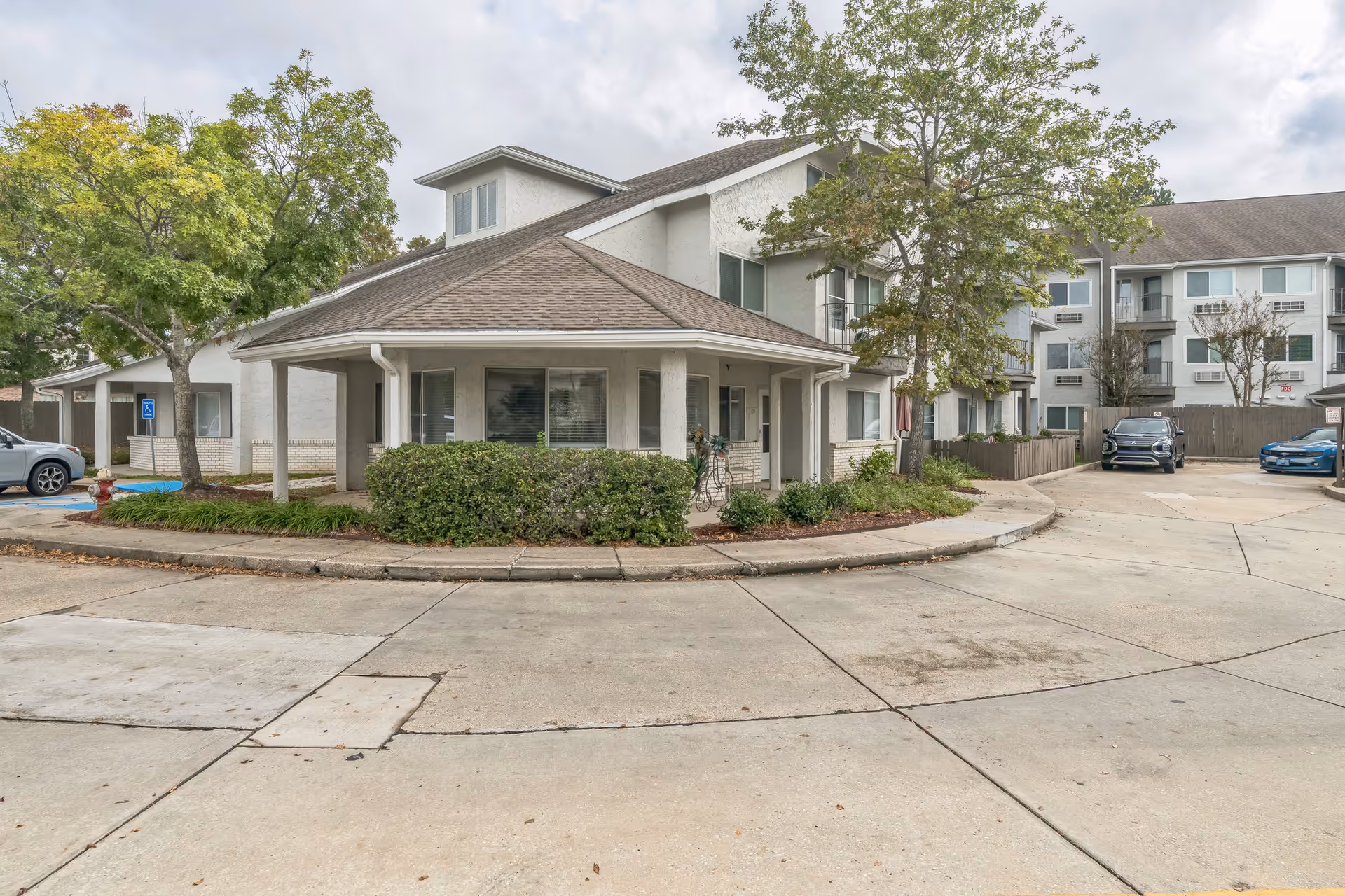 Exterior front of a multi-story senior living building with a covered entrance, landscaping, and parked cars.
