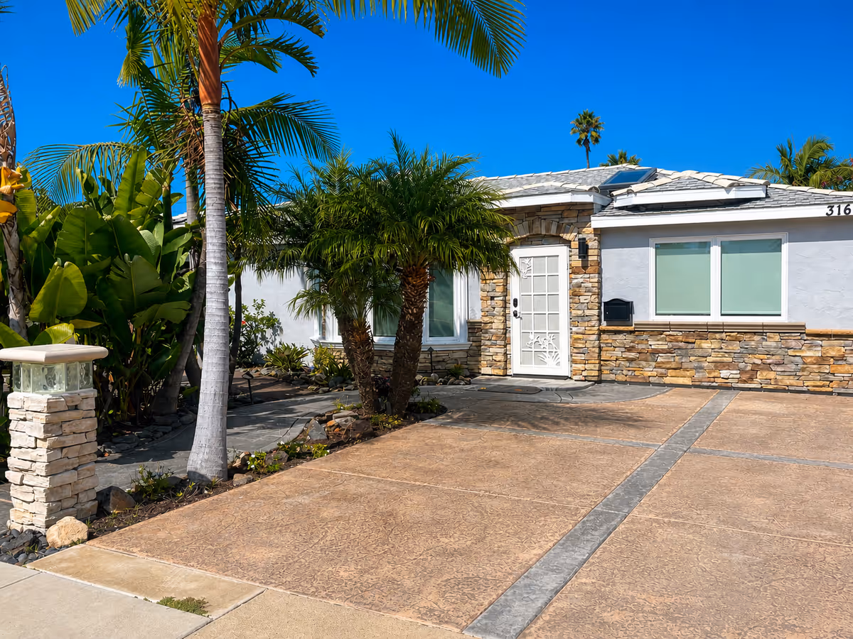 Sunny exterior view of Boutique Care Senior Living facility with palm trees and stone facade.
