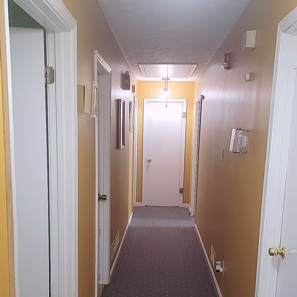 Narrow beige corridor with closed doors and a bright light at the end.