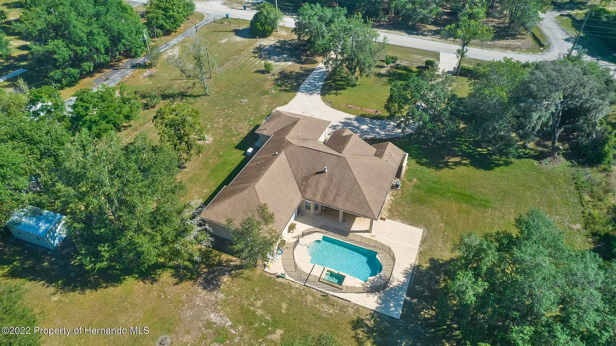 Aerial view of a brown-roofed assisted living facility with a curved pool and green grounds
