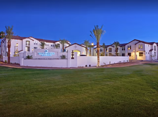 Exterior view of Villa Hermosa senior living campus at dusk with palm trees and green lawn.