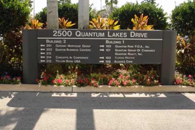 Outdoor building-front sign displaying address and directory, set among colorful flowers.