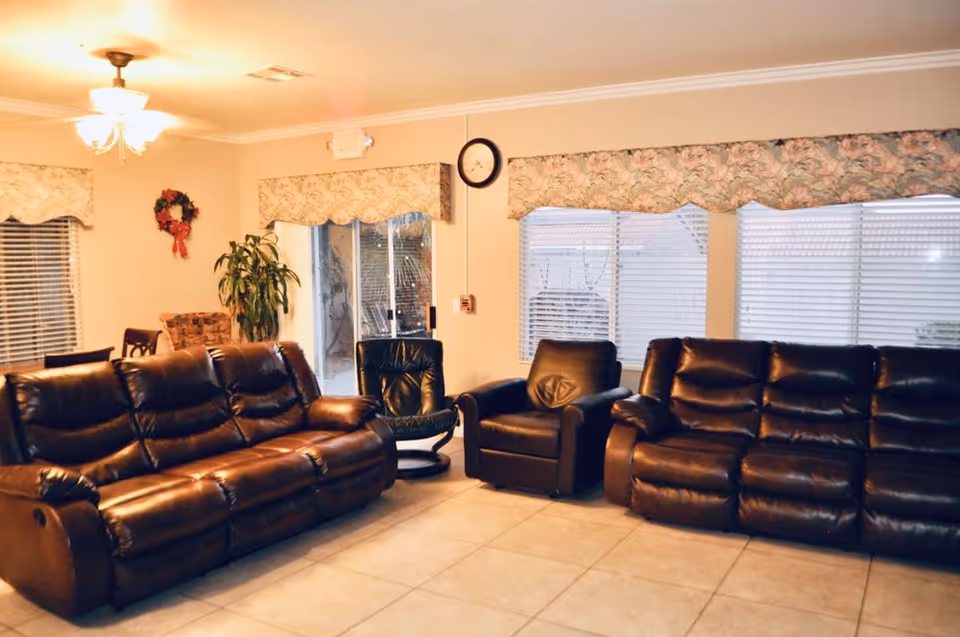 Pleasant Valley Home Care common area: spacious living room with brown leather sofas, windows, and plants.