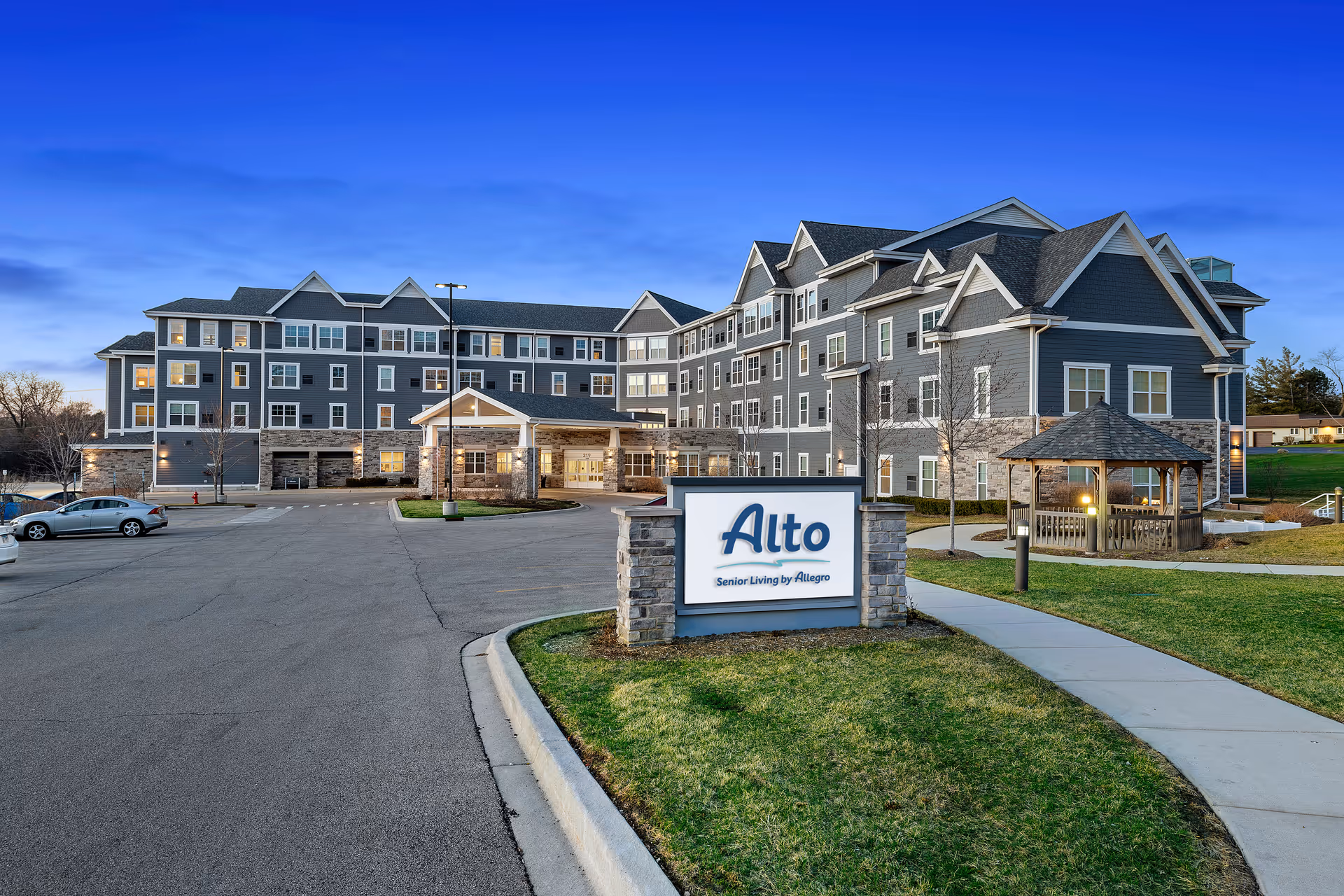 Front exterior of the Alto senior living building with a driveway, gazebo, and a sign in the foreground.