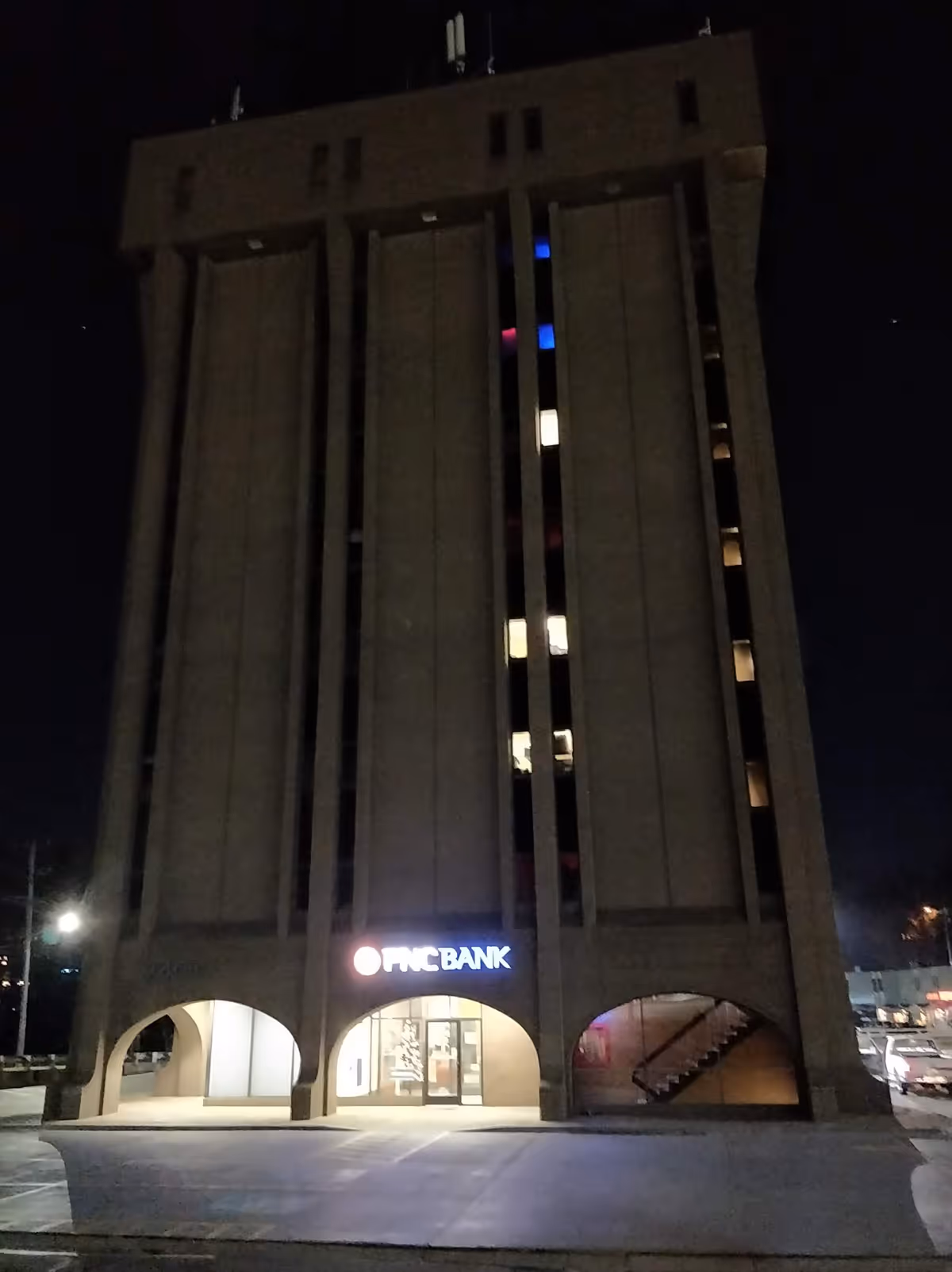 Tall dark multi-story building at night with illuminated arches and an OfficeBank entrance.