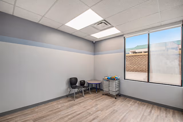 Empty therapy room with chairs, a small table, and a cart by the window.