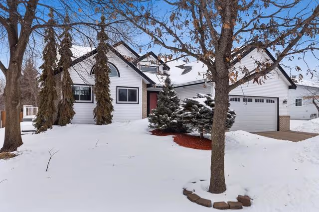 Snow-covered suburban house with a two-car garage and trees in the front yard