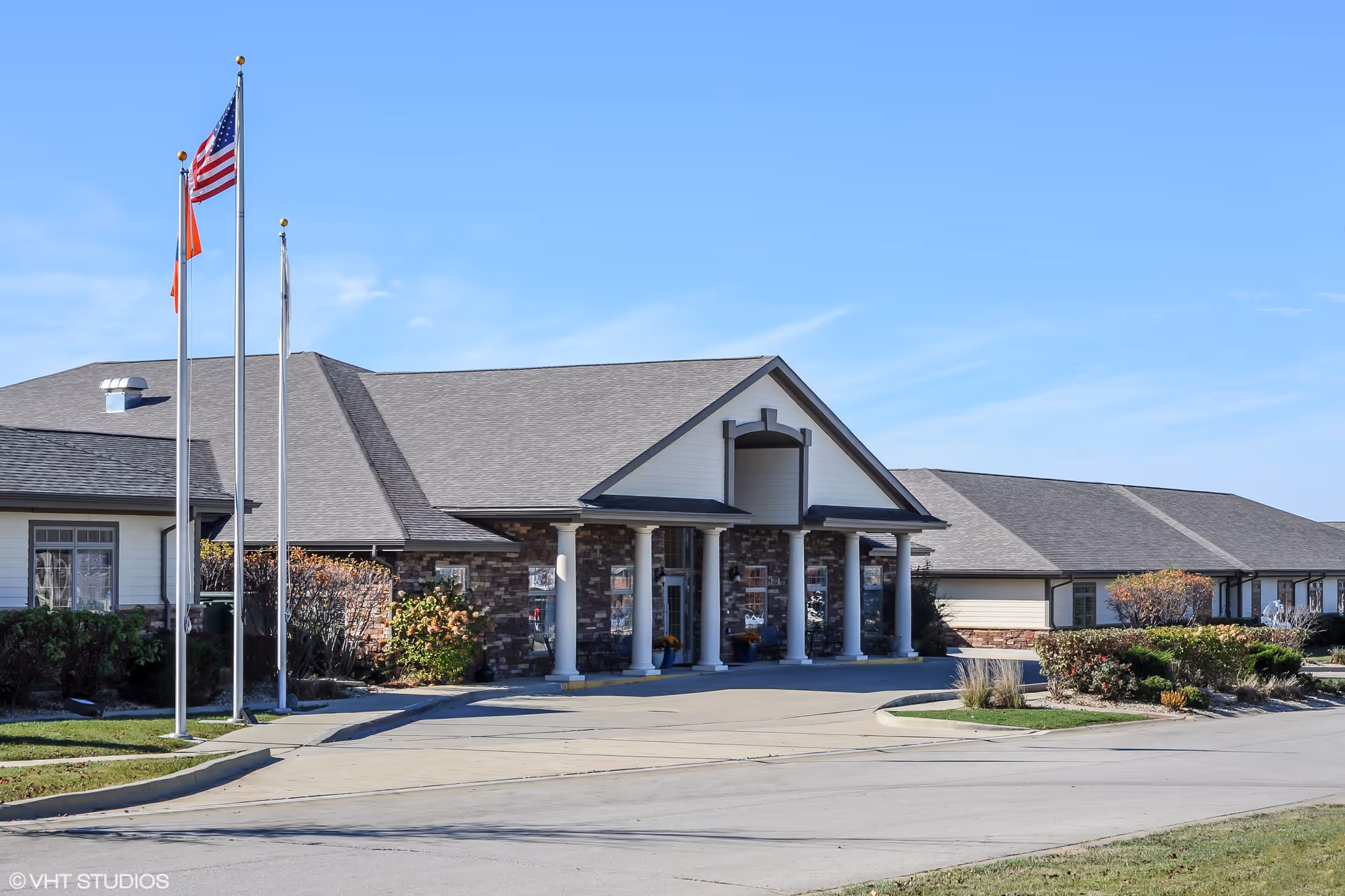 Exterior view of Bridle Brook Assisted Living & Memory Care Community with flagpoles and entrance.