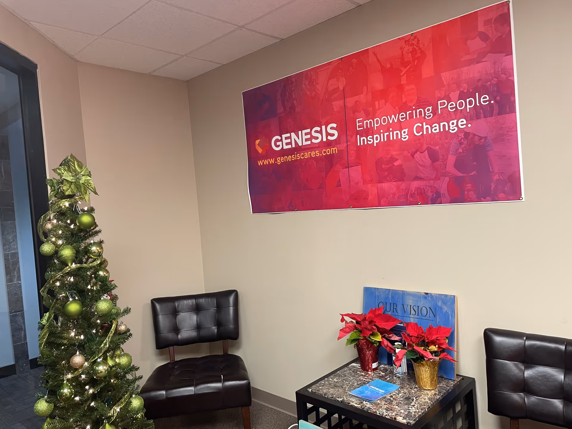 Lobby seating area with a Christmas tree, banner, and poinsettias against beige walls.