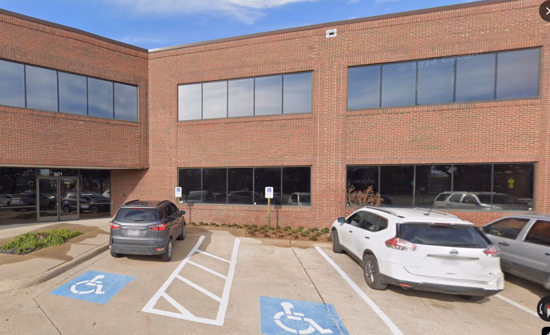 Brick building facade with large windows and accessible parking spaces in front.