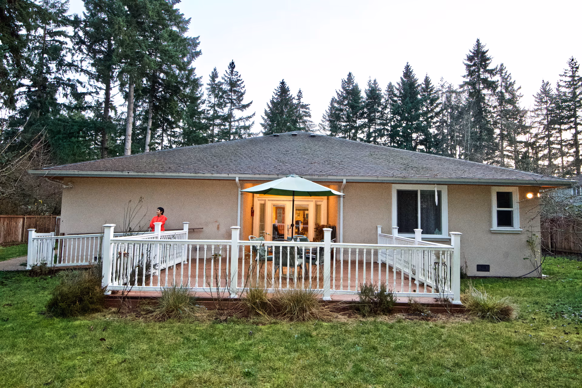 Single-story beige house with a spacious wooden deck and outdoor seating under an umbrella.