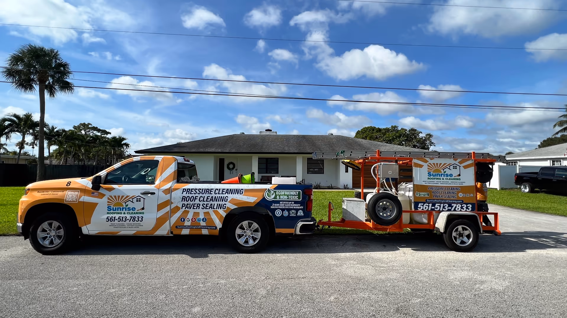 Orange and white service truck with trailer on a residential street in front of a house.