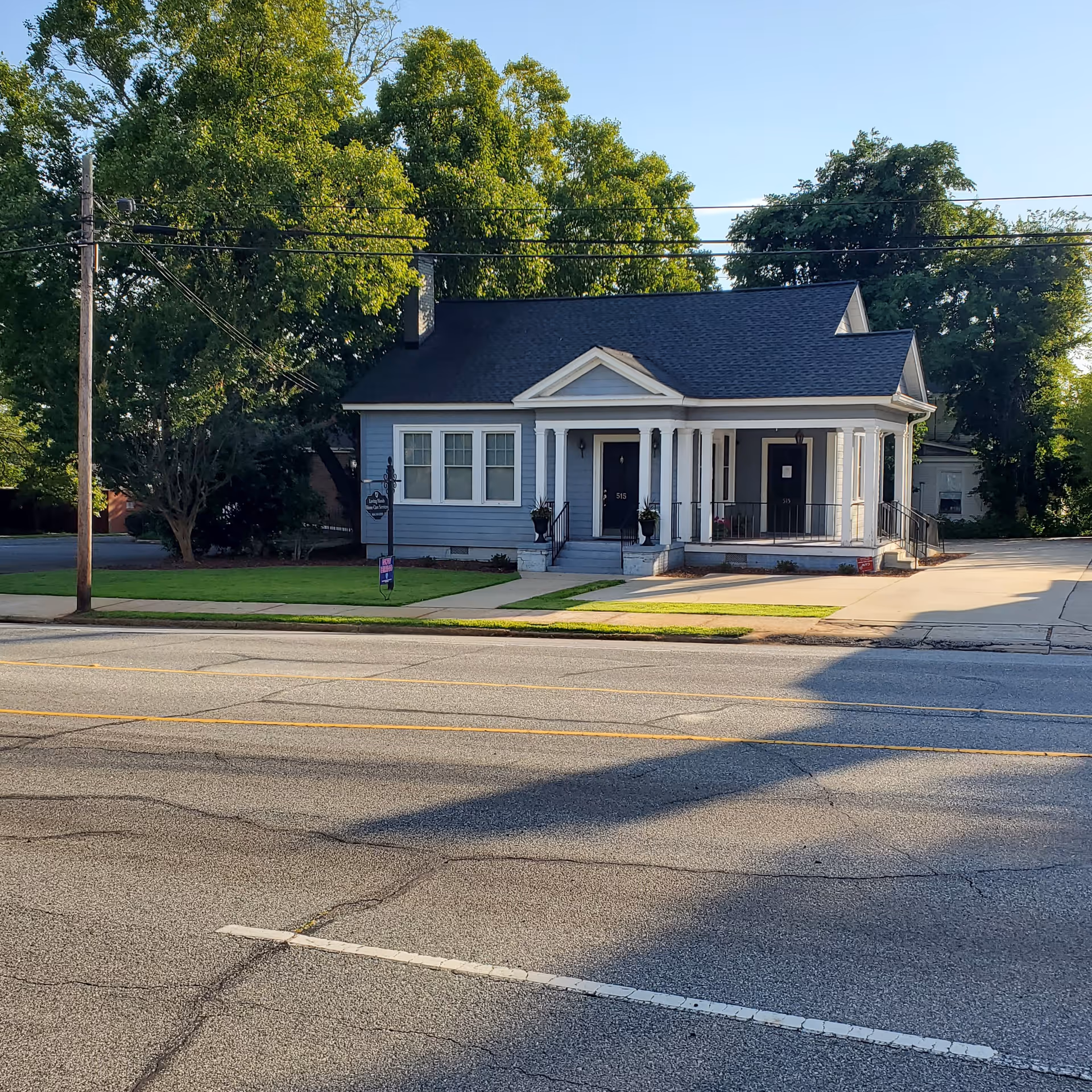 Blue, single-story building with a covered front porch and columns on a sunny street.