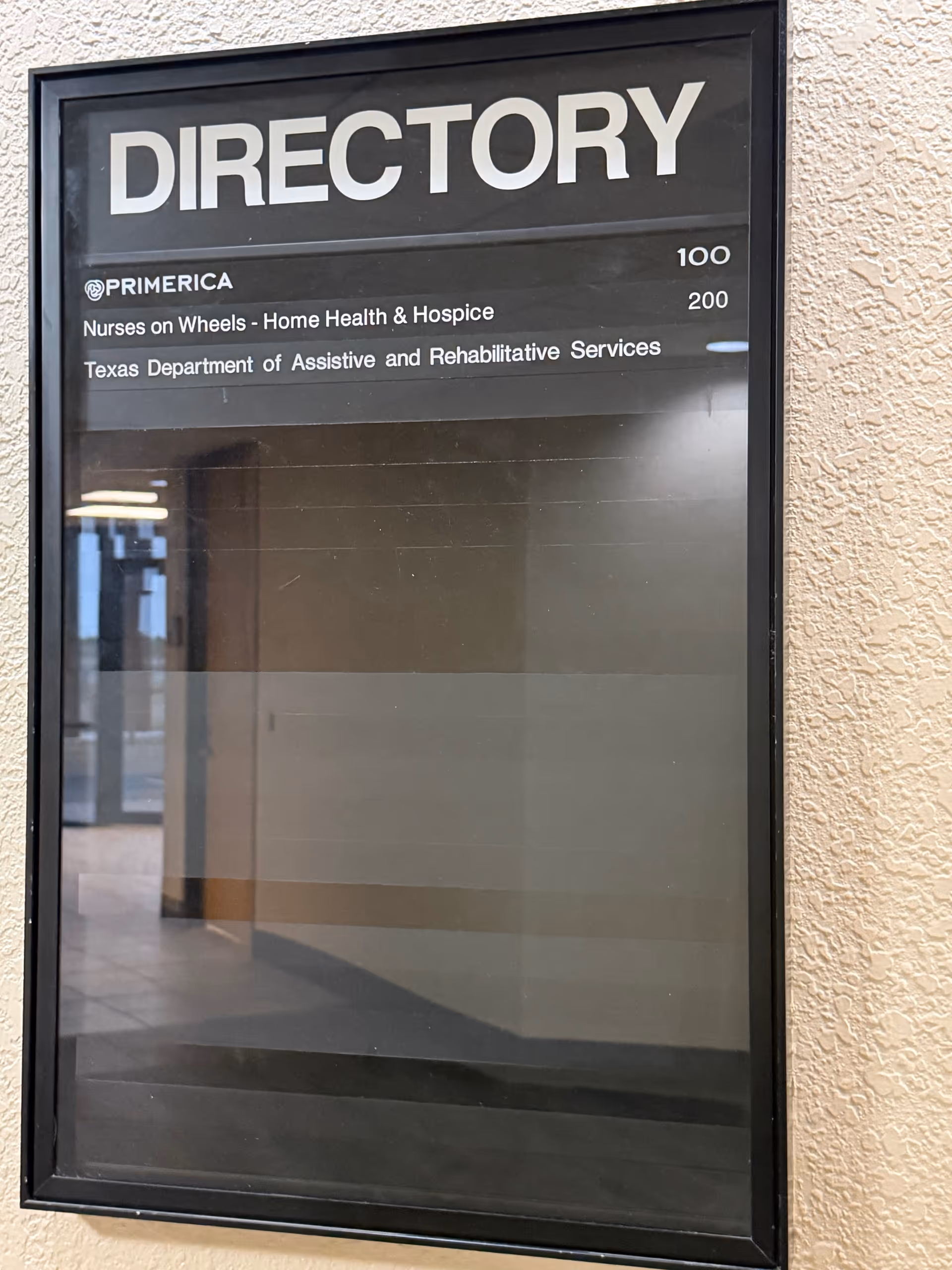 Exterior directory sign on beige wall listing Nurses on Wheels and health services.