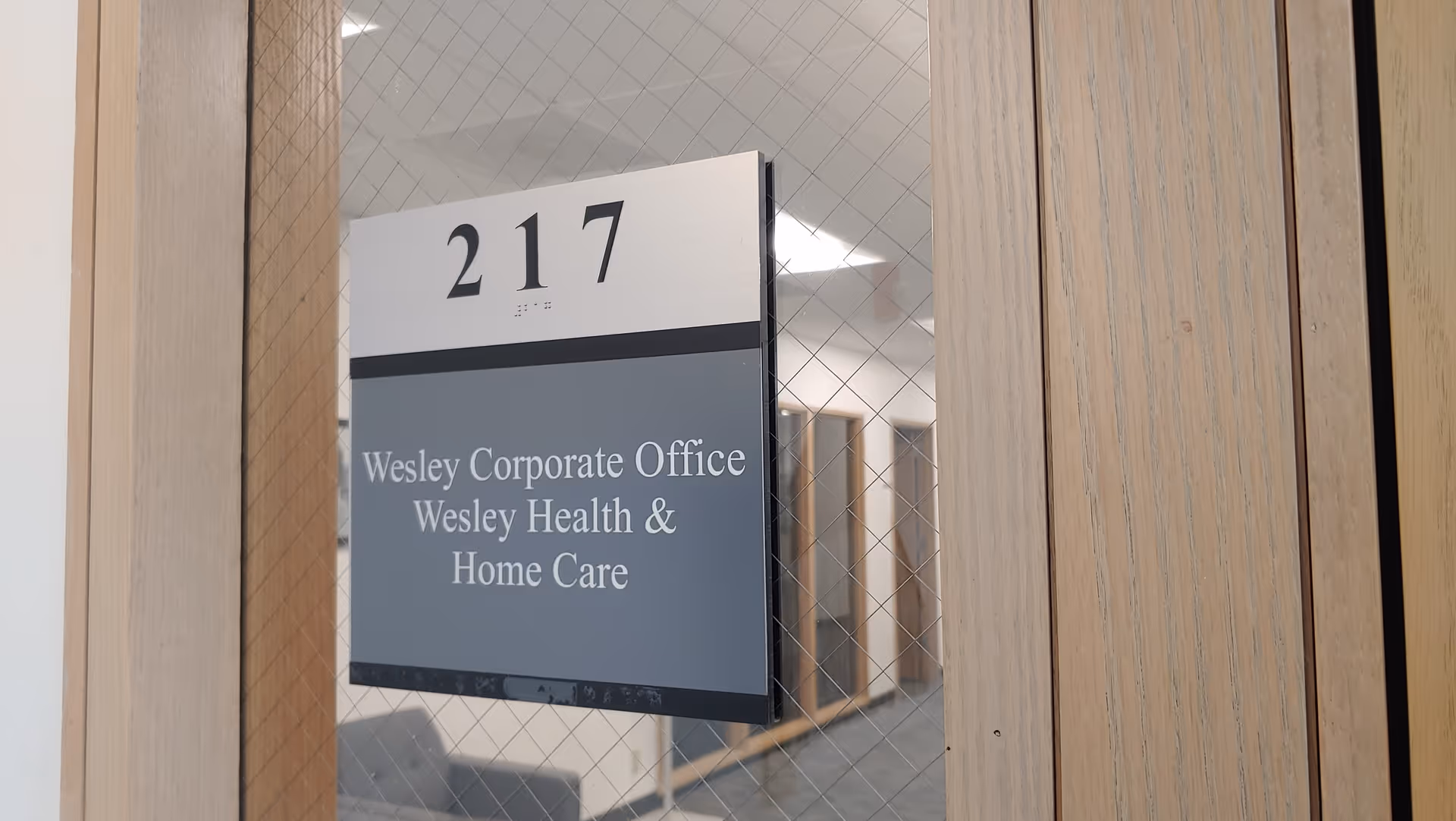 Door with windowed panel and sign reading Wesley Corporate Office, 217, inside a hallway.