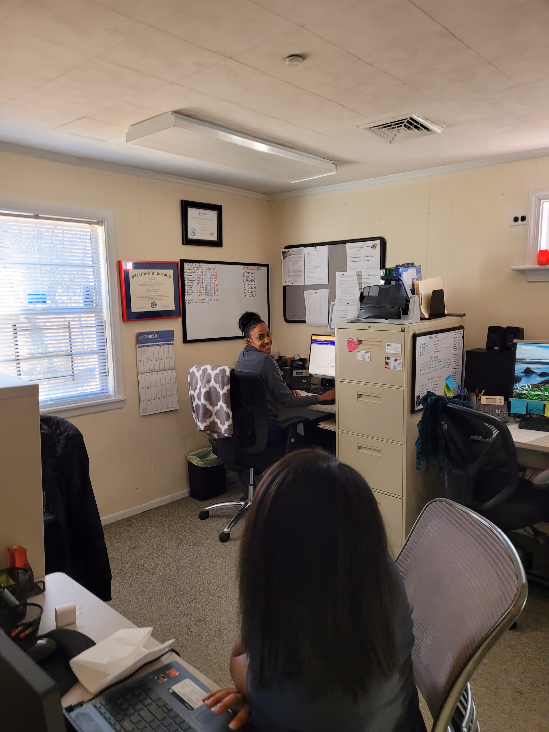 A staff member smiles while working at a desk in a small office.