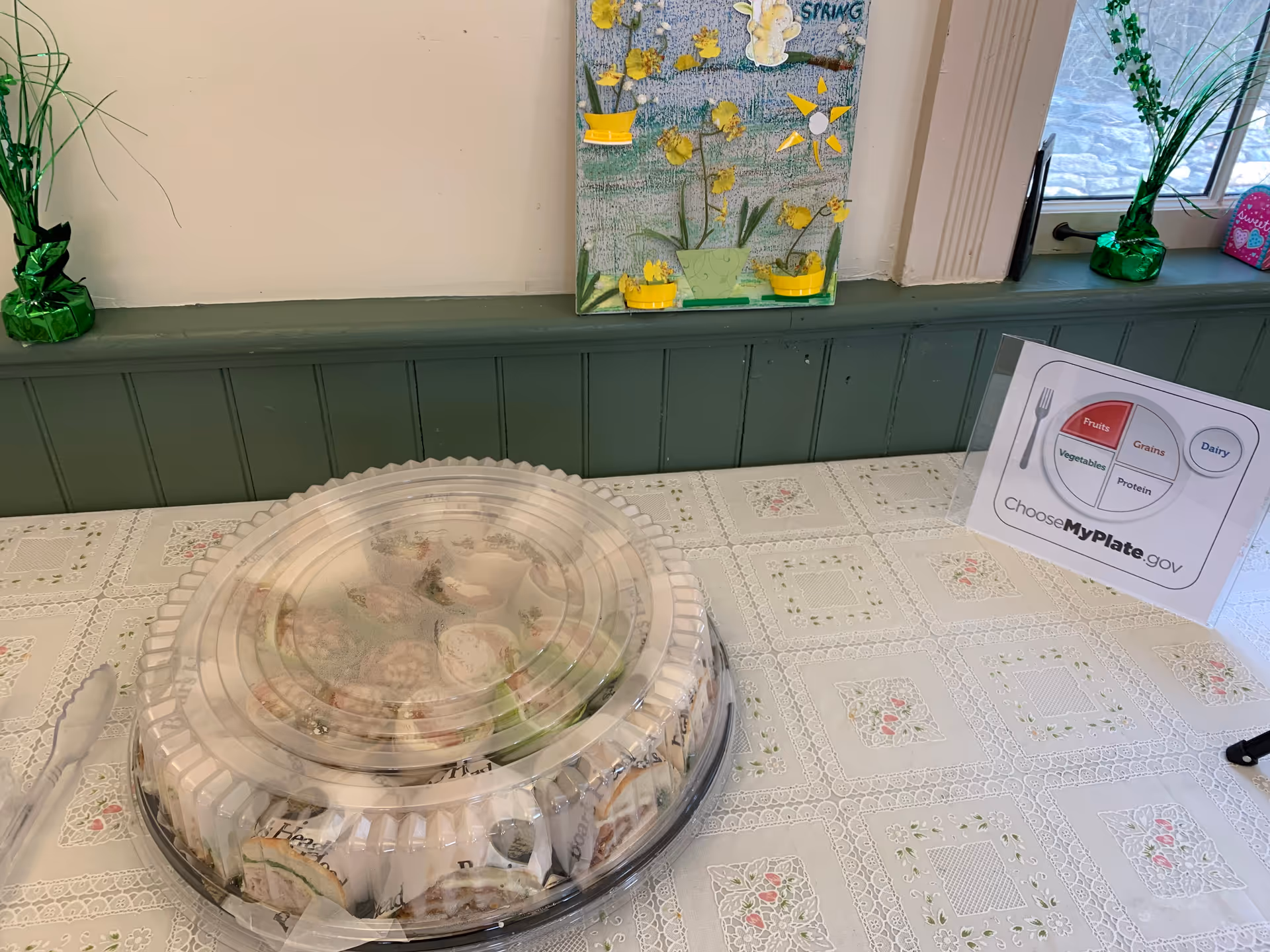 Large plastic-covered platter on a lace-draped dining table with a nutrition sign.