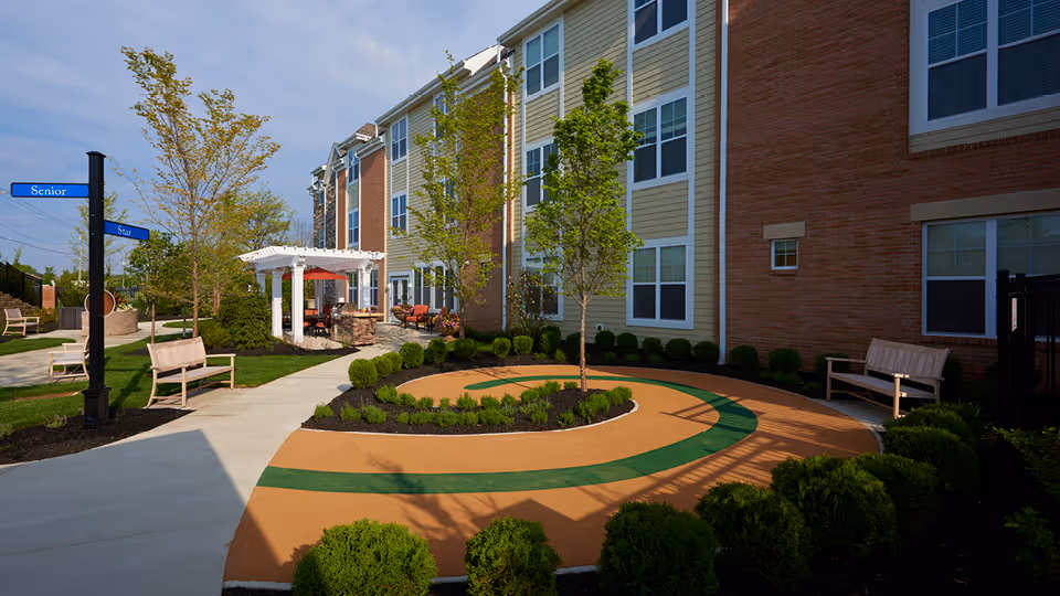 Exterior view of a senior living courtyard with circular path, benches, and trees.
