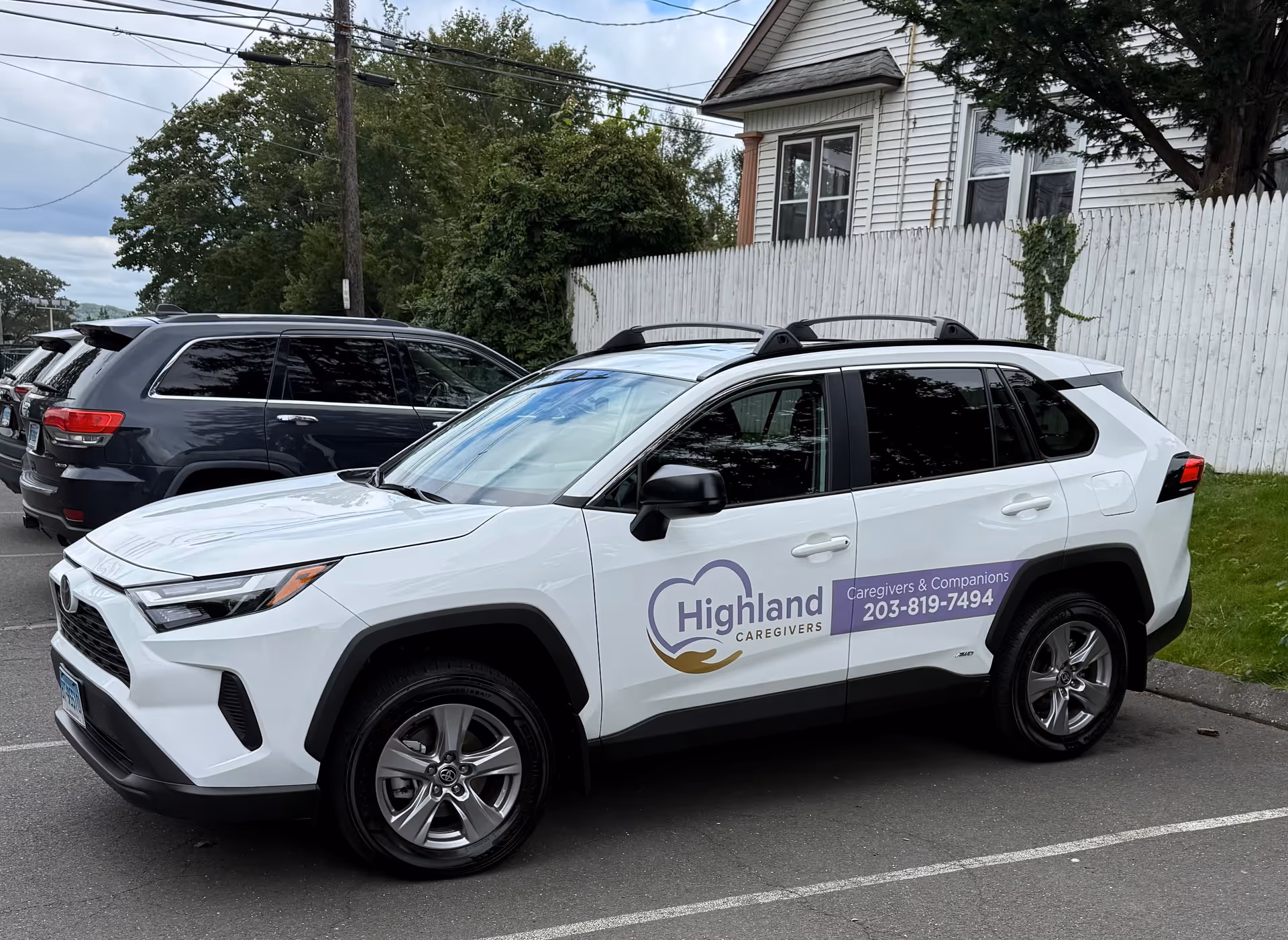 White Highland Caregivers SUV parked in a lot beside a white fence.