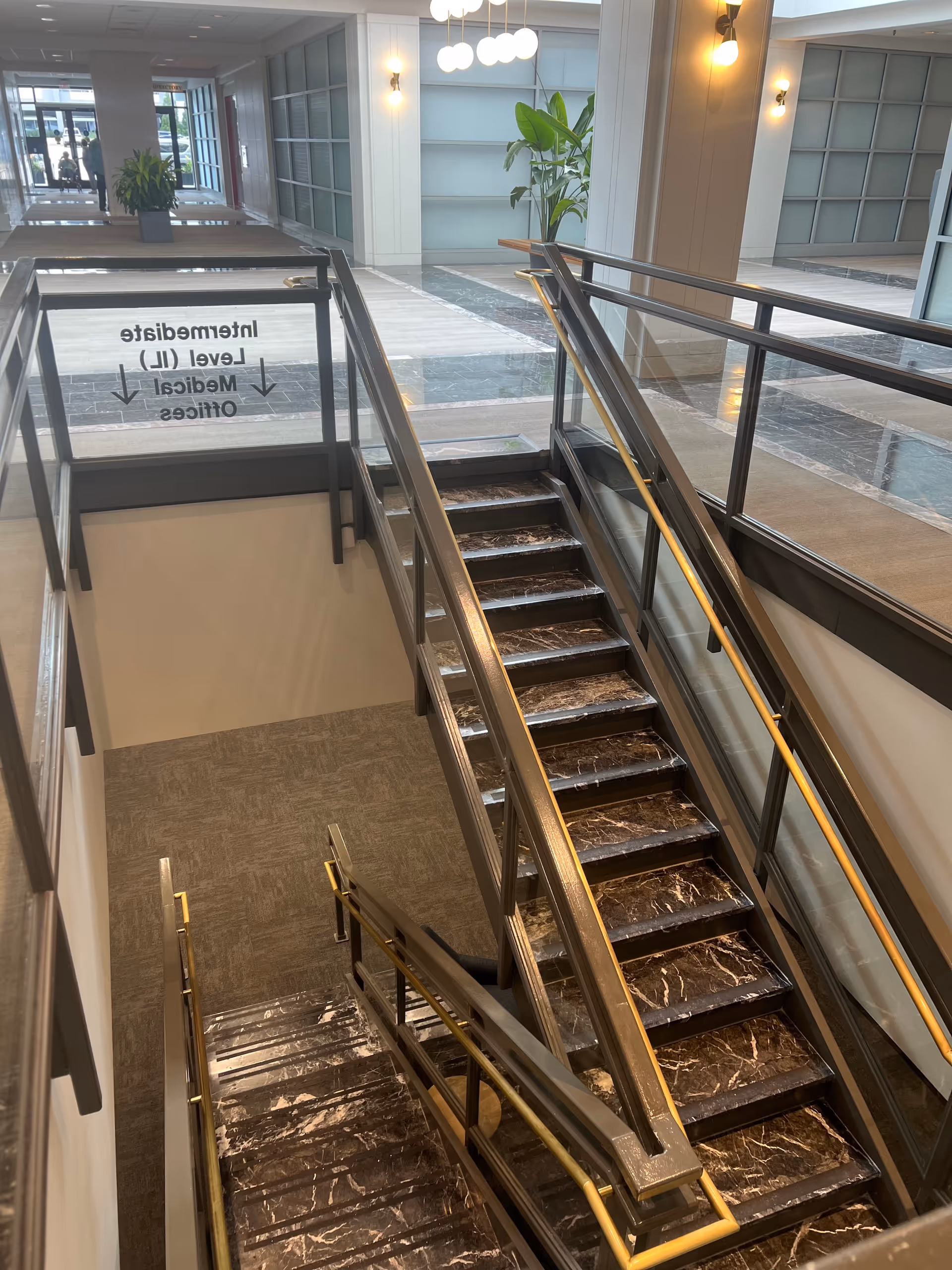Inside a modern senior living facility: a wide stairwell and glass-walled hallway.