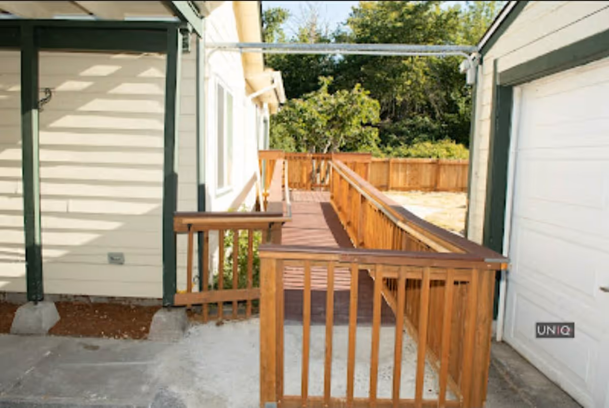 Outdoor view of a wooden wheelchair ramp with handrails between beige buildings.