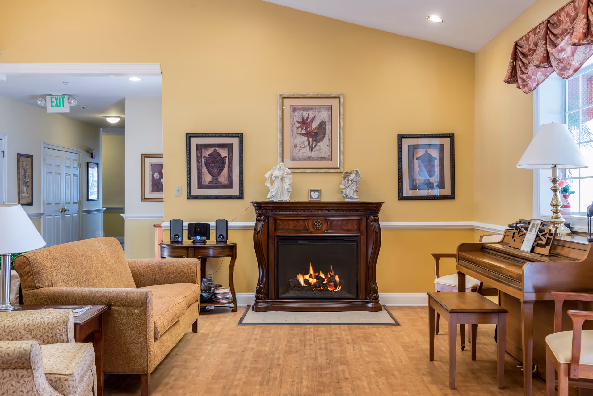 Cozy living room at Sagepoint Gardens Assisted Living with a fireplace, piano, and seating.