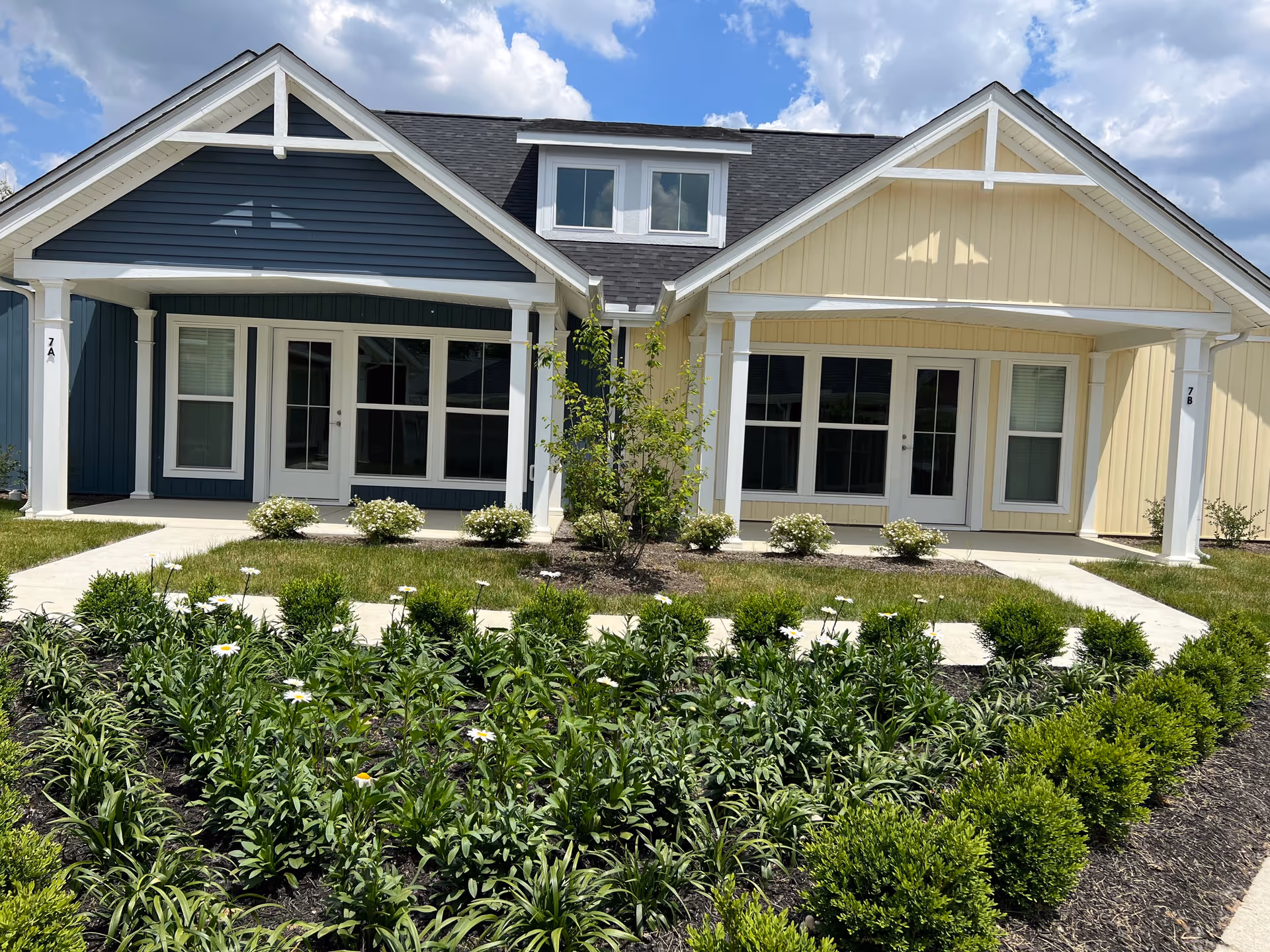 Exterior view of The Hamlet on Darby with blue and beige siding and landscaped flower beds.