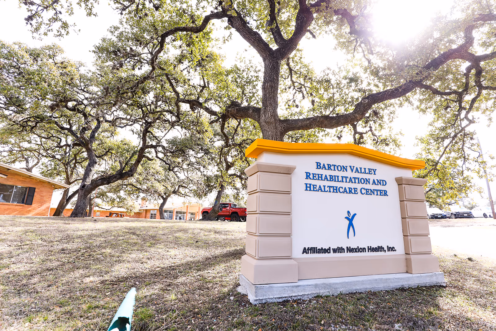 Outdoor view of a stone sign for Barton Valley Rehabilitation and Healthcare Center under oak trees.