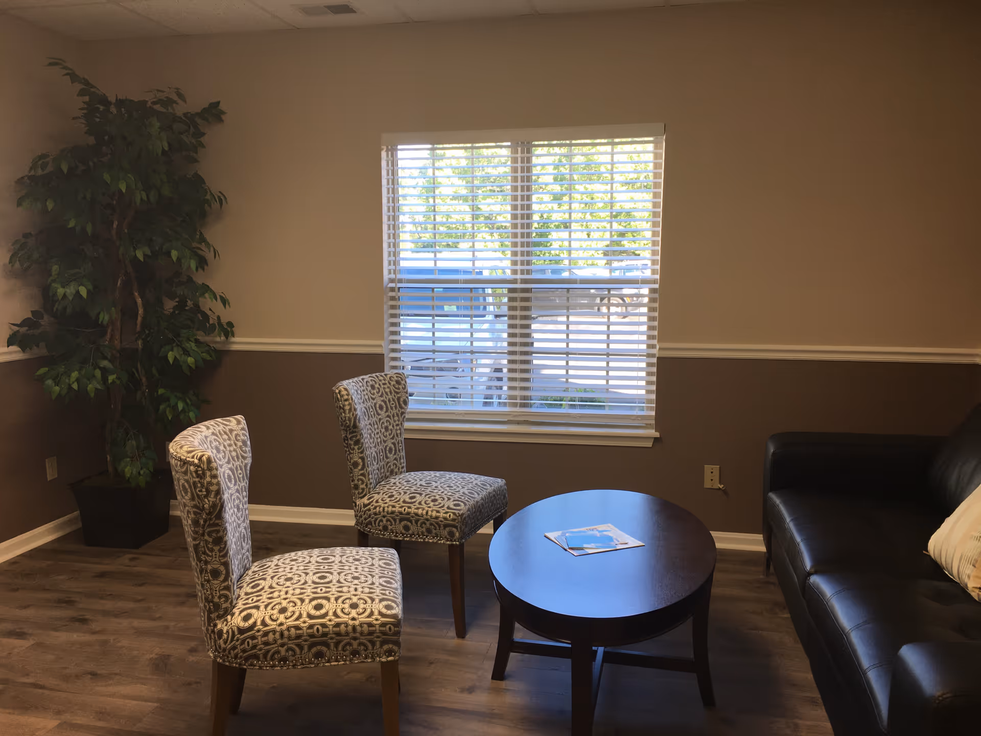 Small living room lounge with two patterned chairs, a round coffee table, and a leather sofa.
