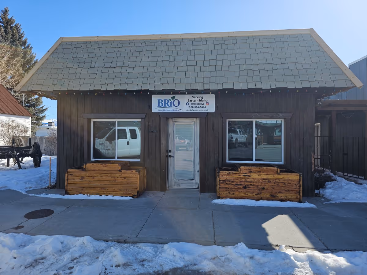 Small wooden facility front with BRiO Home Health and Hospice sign, snow around planters.