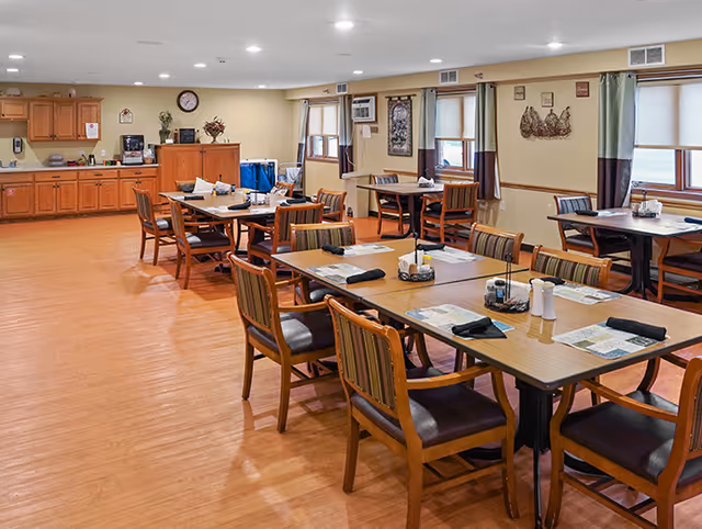 Empty communal dining room with multiple tables and chairs in a senior living facility.