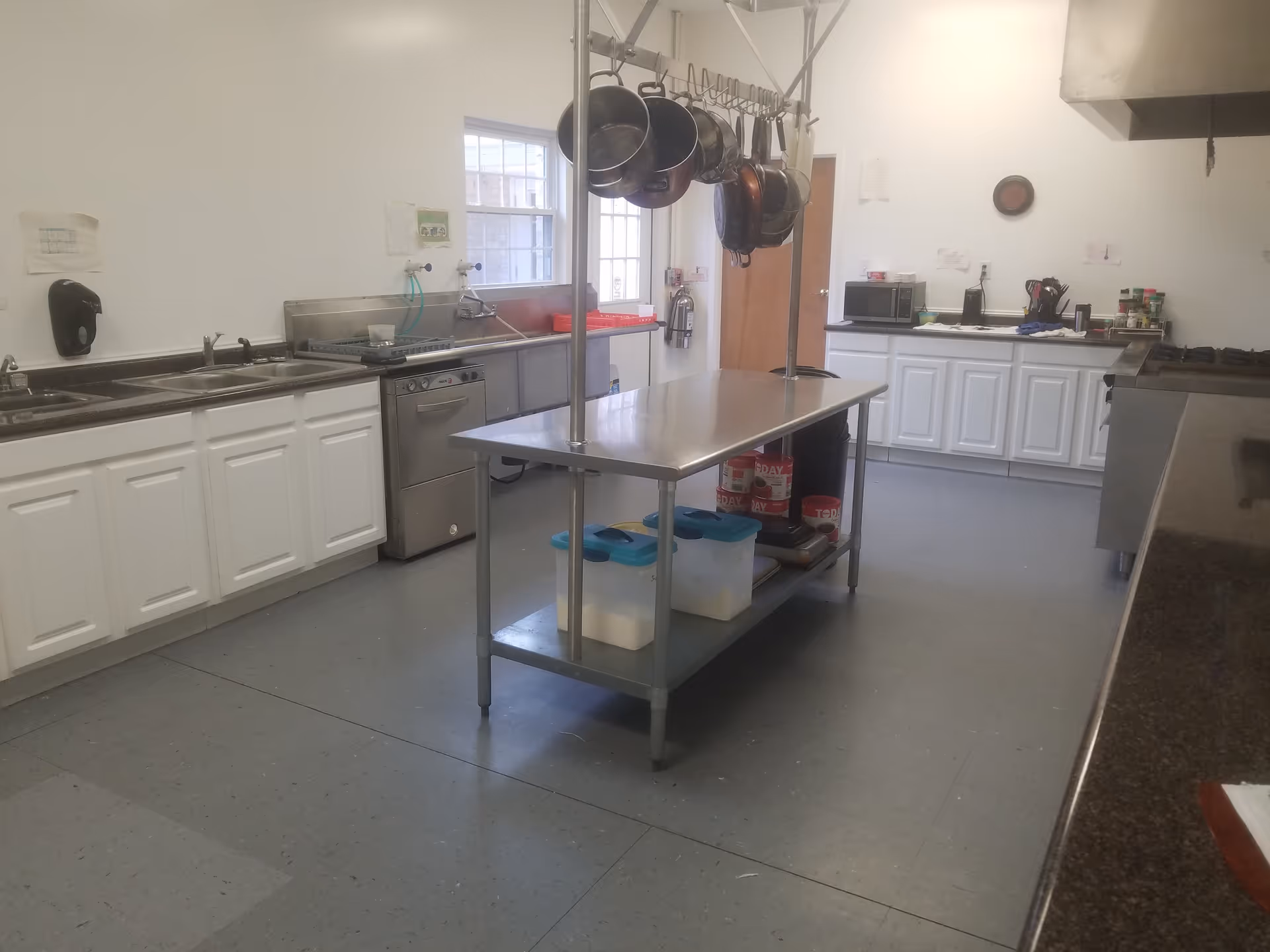 Commercial kitchen in Henderson Villa with stainless island, hanging pots, and white cabinets.