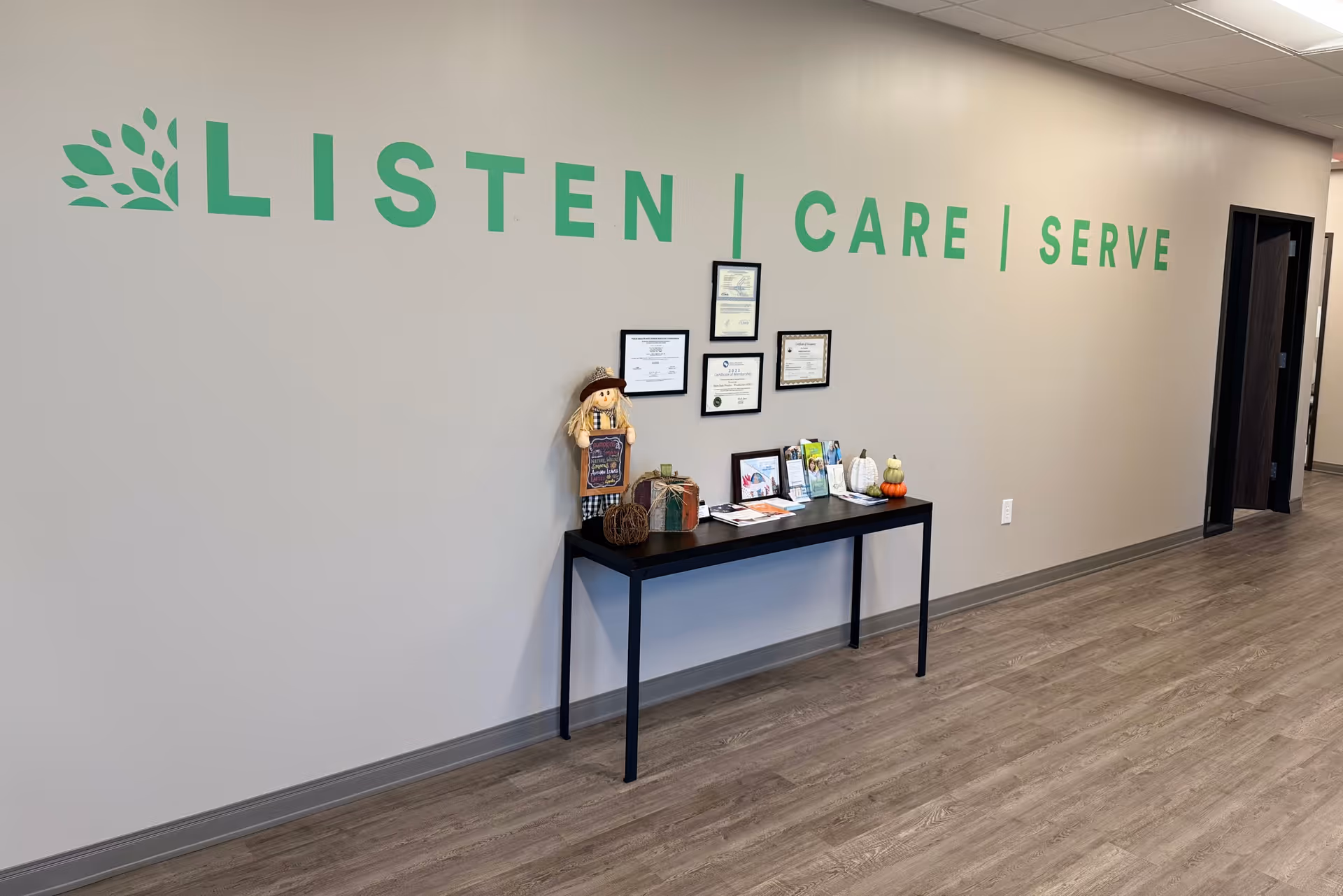 Indoor hallway with a wall slogan LISTEN CARE SERVE and a decorated table.