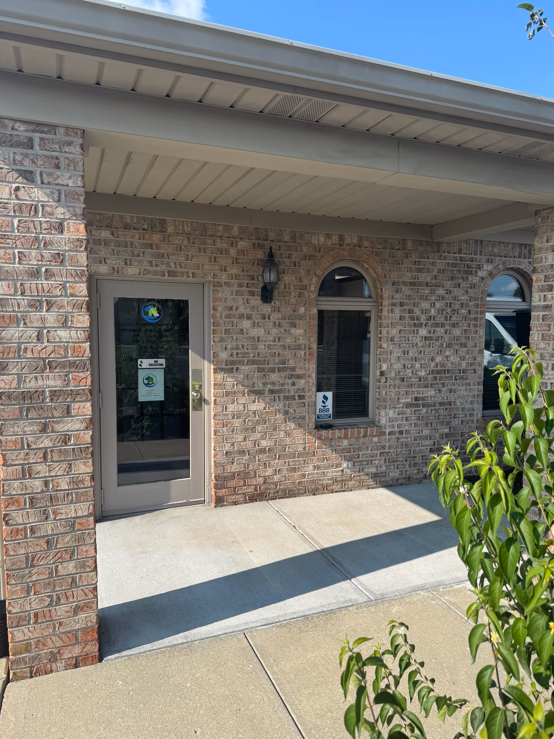 Brick facility entrance with glass door, arched windows, and a concrete sidewalk.